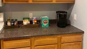 Een keuken met houten kastjes, een granieten aanrechtblad en diverse keukenbenodigdheden, waaronder een koffiezetapparaat, een pak ontcafeïneerde koffie en wat kruiden.