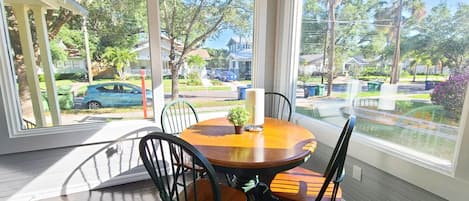 A sunroom with a wooden table and chairs, large windows, and a view of a residential street.