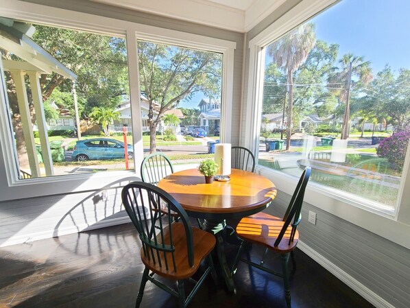 A sunroom with a wooden table and chairs, large windows, and a view of a residential street. - Best Location in Hyde Park, South Tampa (Tampa)