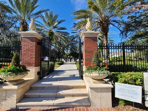 A gated entrance with a pathway leading to a park area, featuring palm trees and flower beds. - Best Location in Hyde Park, South Tampa (Tampa)