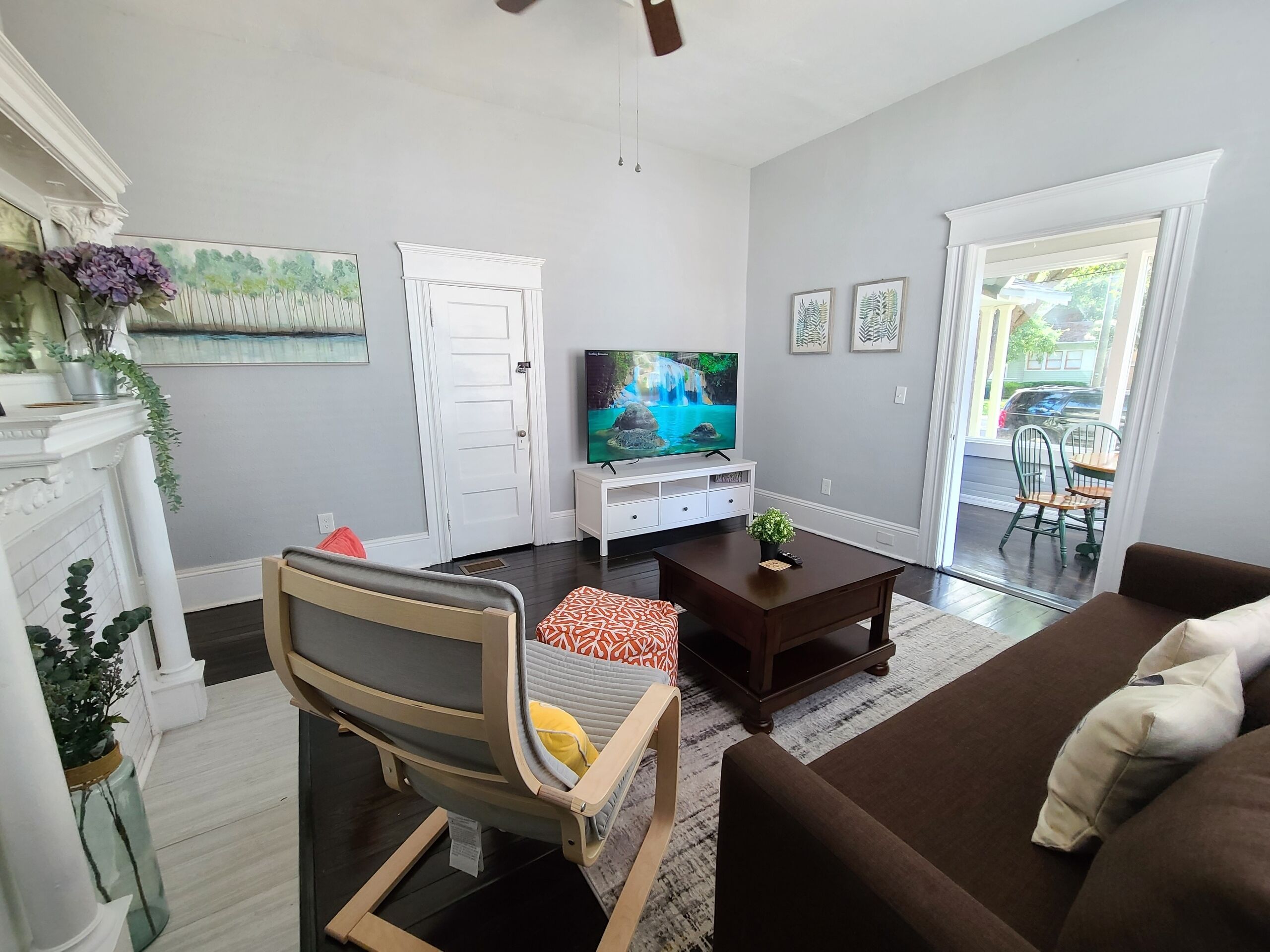 A living room with a sofa, a chair, a TV on a stand, a fireplace, and a door leading to a balcony.