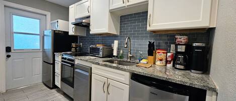 A modern kitchen with stainless steel appliances, white cabinetry, and a black tiled backsplash.