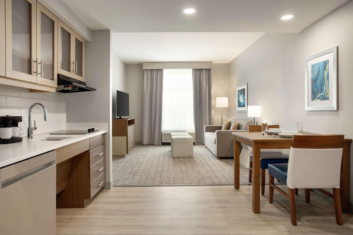 Una cocina moderna con horno empotrado, un comedor con mesa y sillas de madera, y una sala de estar con sofá y televisor.