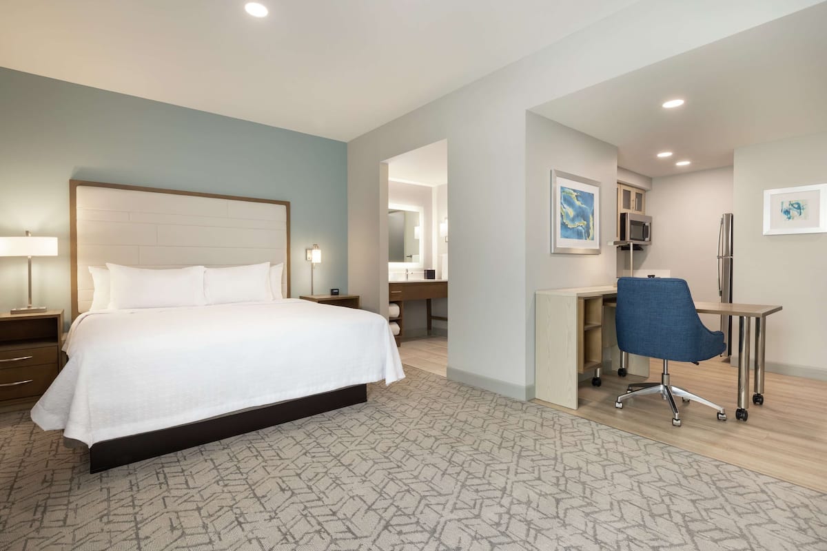 Una habitación de hotel con una cama grande, un escritorio con silla, un microondas y un refrigerador.