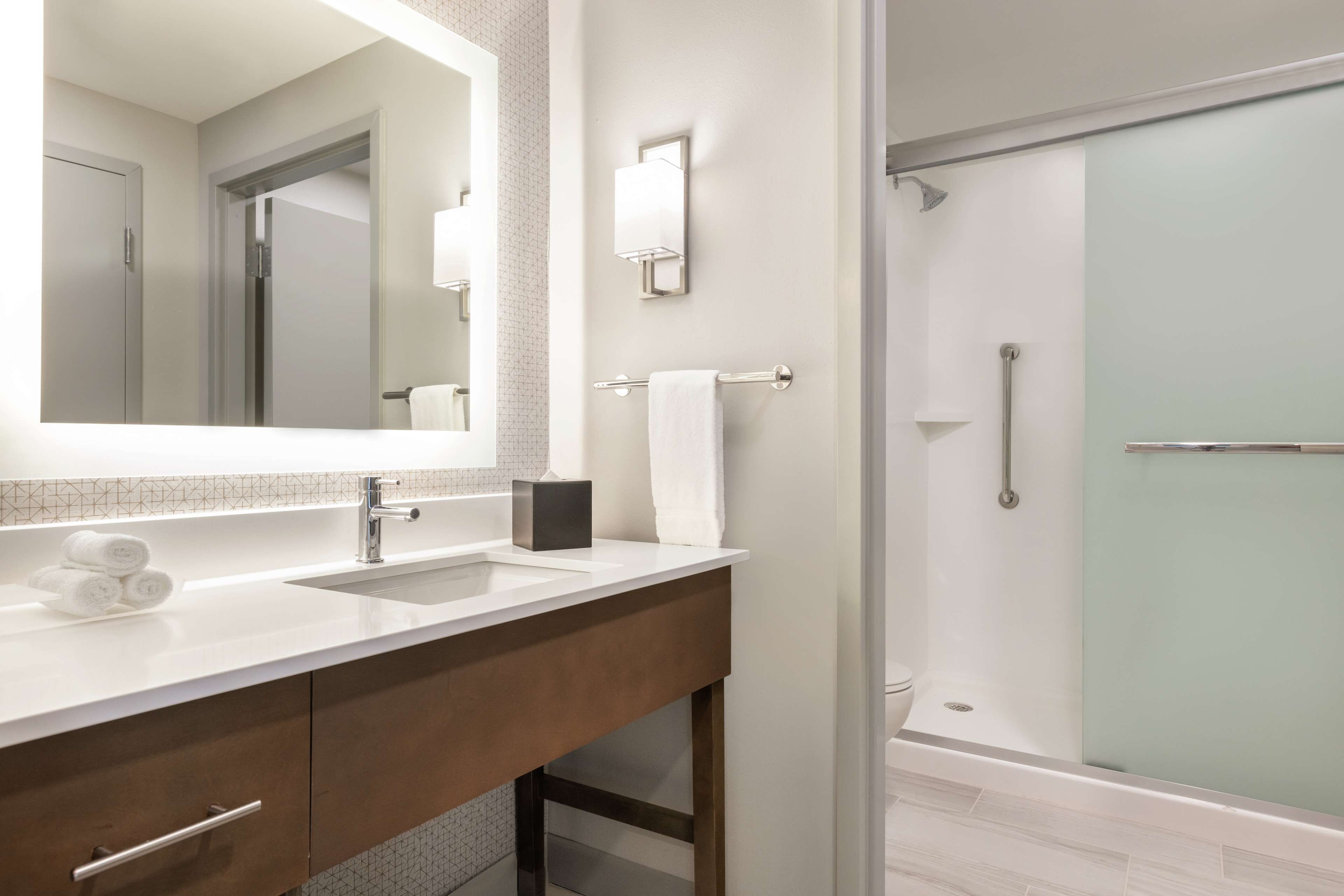 A modern bathroom with a large mirror, dual sinks, a towel rack, and a glass-enclosed shower.