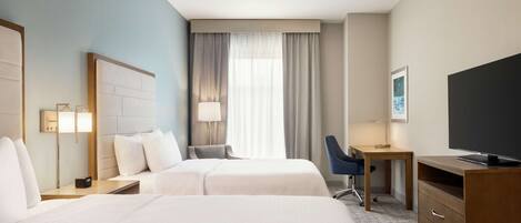 Une chambre d’hôtel avec deux lits, un bureau, une chaise, une télévision et une fenêtre avec des rideaux.