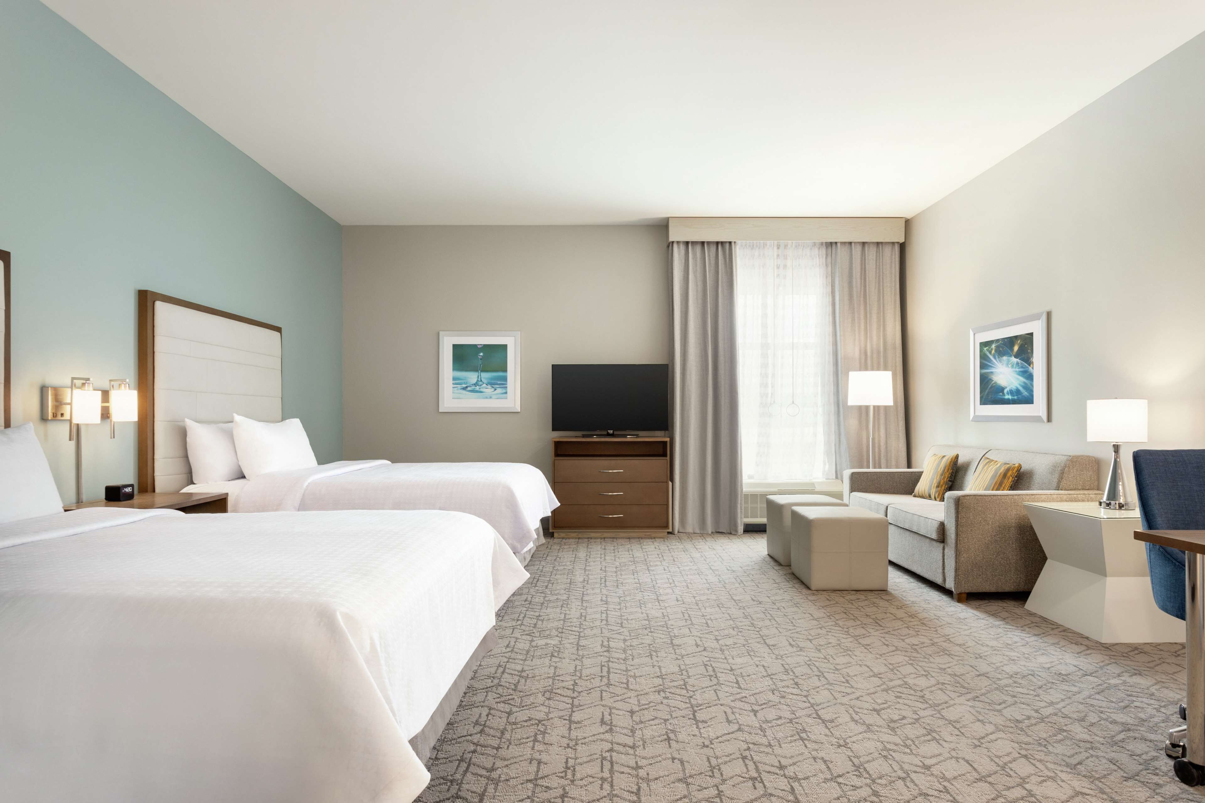A hotel room with two beds, a TV, a desk with a chair, and a sofa.