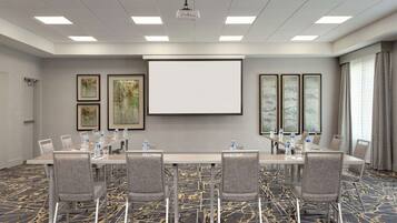 A conference room with a long table, chairs, a projector screen, and framed artwork on the walls.