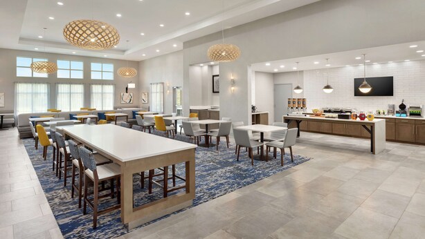 Un comedor de hotel moderno con varias opciones de asientos, incluidas mesas y sillas, y una zona de cocina con bar.