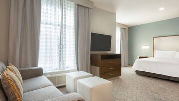 Habitación de hotel con sofá, otoman, televisor de pantalla plana, cama y mesita de noche con lámpara.
