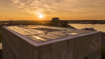 Un bâtiment moderne doté d’un toit plat et de grandes fenêtres, offrant une vue sur une étendue d’eau et un coucher de soleil.