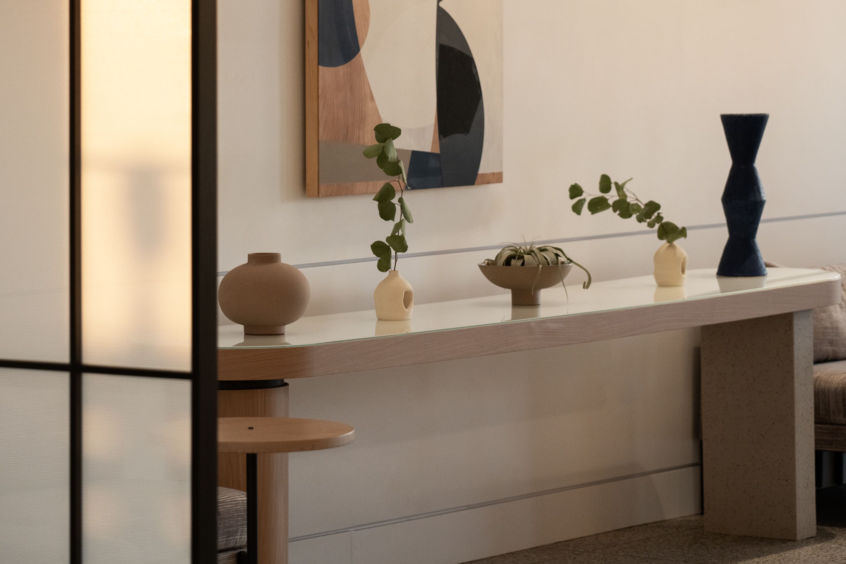 A modern interior with a minimalist design, featuring a long, low-profile table with decorative vases and a potted plant.