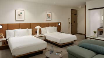 Habitació d'hotel amb dos llits, un sofà verd, una taula petita i obres d'art a les parets.