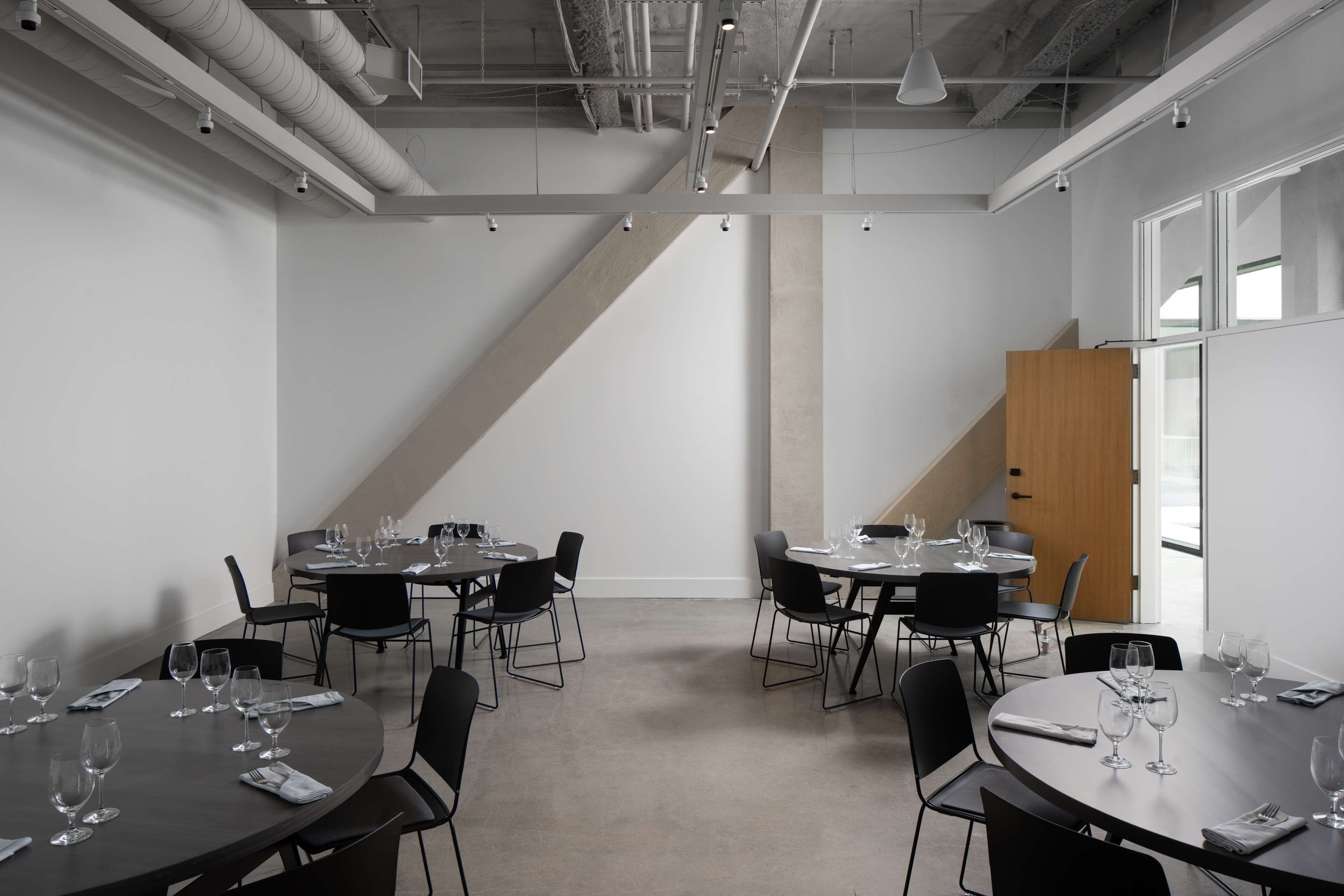 Une salle de conférence moderne, dotée de tables rondes, de chaises noires et de présentoirs en verre.