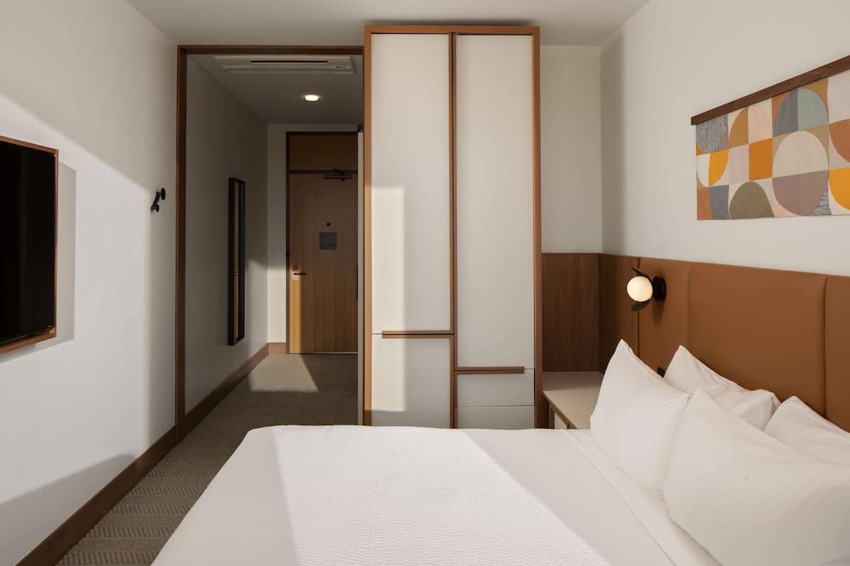 A hotel room with a large bed, a wooden headboard, a wall-mounted TV, and a door leading to another room.
