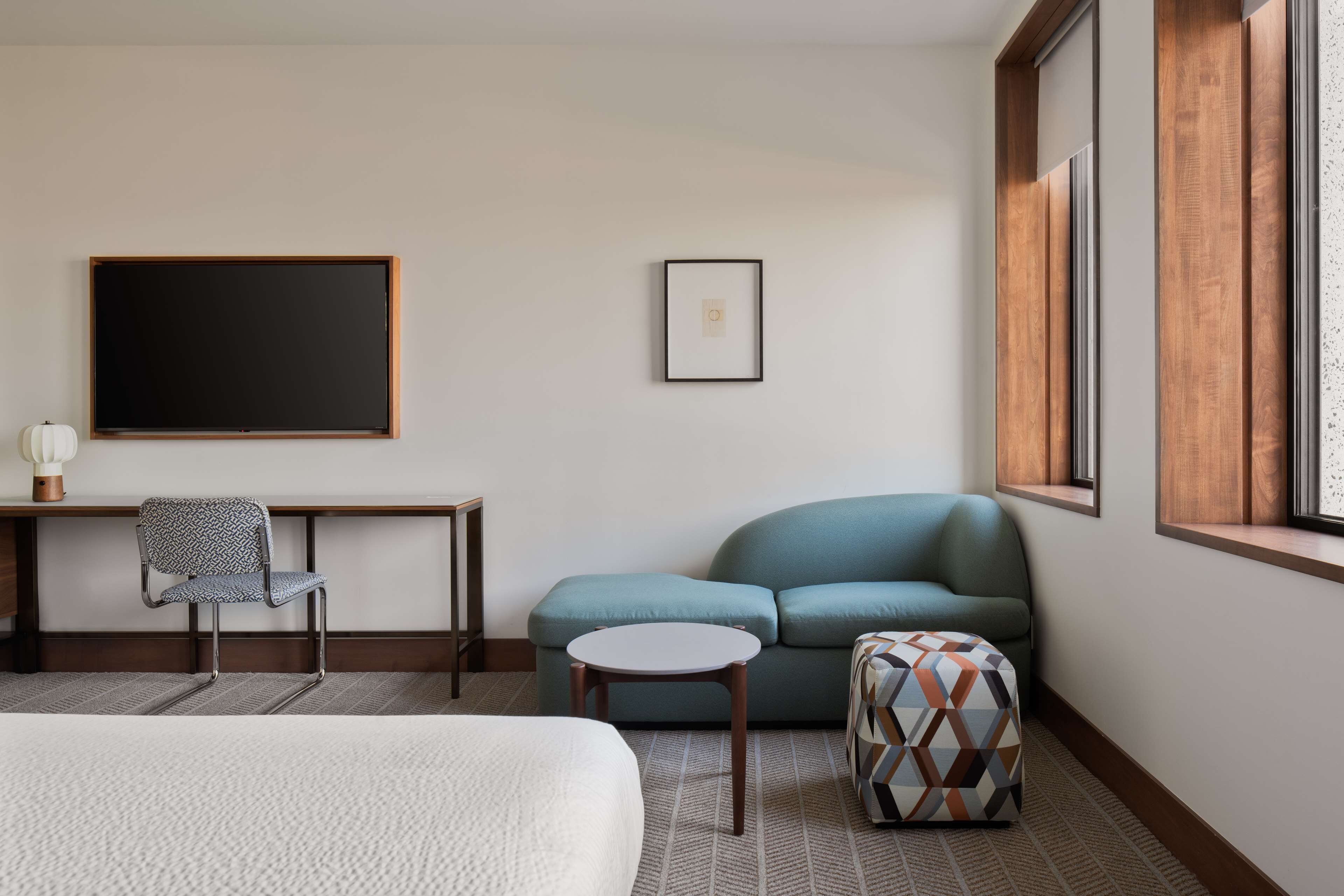 A hotel room with a bed, a desk, a chair, a sofa, a small table, and a window.