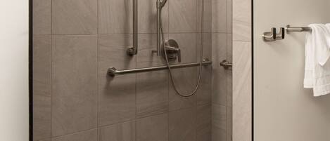 A shower area with a grab bar, a handheld showerhead, and a towel rack.