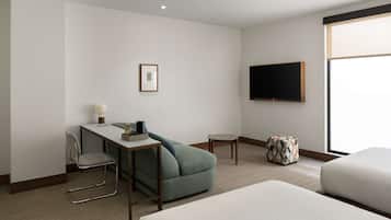 Una habitación de hotel con cama, escritorio, silla, televisor en la pared y ventana.
