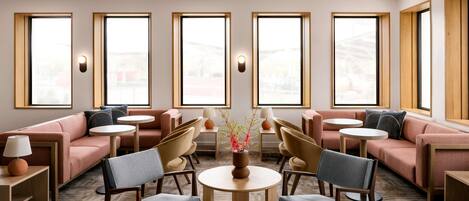 A modern lounge area with sofas, chairs, and tables arranged around large windows.