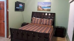 A bedroom with a bed, a ceiling fan, a TV, and a painting on the wall. - Maryville Studio (St.Thomas)