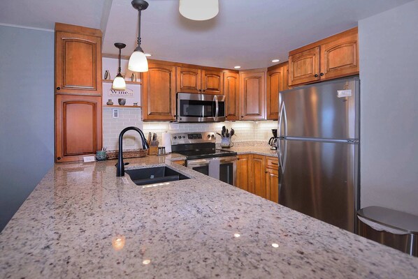 A kitchen with granite countertops, stainless steel appliances, wooden cabinets, and pendant lighting.