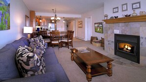 A living room with a fireplace, a dining area, and a kitchen in the background. - Columbine Slopeside, Ski in/out, Hot tub (Crested Butte)