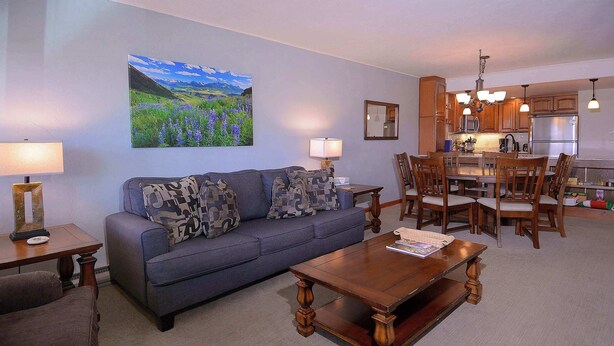 A living room with a sofa, coffee table, and dining area with chairs and a kitchen in the background. - Columbine Slopeside, Ski in/out, Hot tub (Crested Butte)
