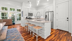 A modern kitchen with white cabinetry, stainless steel appliances, and a central island with bar stools. - Bring Fido! Stylish 4BR Home in Eastern Lake (Santa Rosa Beach)