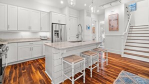 A modern kitchen with white cabinetry, a stainless steel refrigerator, a marble countertop, and a wooden staircase. - Bring Fido! Stylish 4BR Home in Eastern Lake (Santa Rosa Beach)