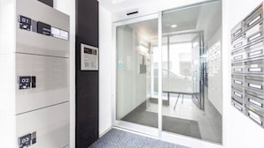 A modern office space with a glass door leading to a conference room, a white wall with numbered storage units, and a carpeted floor. - ORANGE (Sapporo)