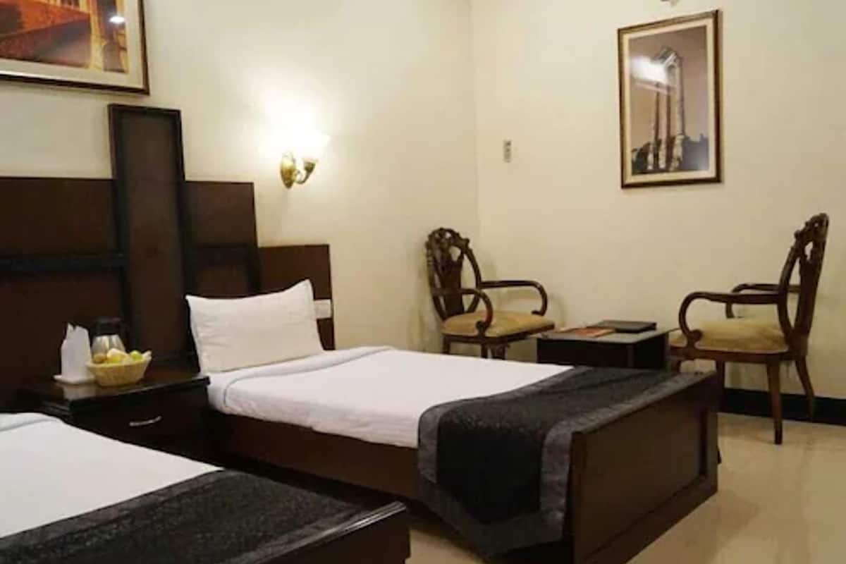 Ein Hotelzimmer mit zwei Betten, einem Nachttisch, einem Sessel, einem kleinen Tisch und einer Wandleuchte.