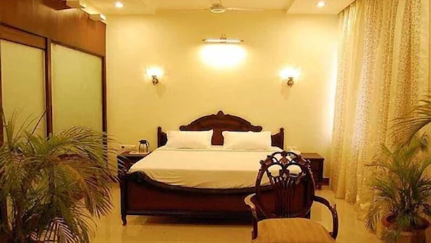 A hotel room with a large bed, two bedside tables, a chair, and two potted plants. - The Avalon Durg (Durg)