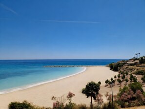 A beach with a clear sky, a sandy shore, and a rocky breakwater.