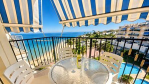 A balcony with a glass table, white chairs, and a view of the sea and buildings. - Sunny Sea View Beachfront, Wi-Fi and Air Conditioning (El Campello)