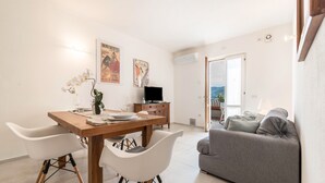 A modern living room with a dining area, a grey sofa, and a TV. - Appartamento "Le Cementine" with Lake View, Mountain View, Wi-Fi, A/C & Terrace (Vesio, Tremosine sul garda)