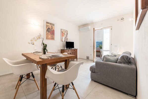 A modern living room with a dining area, a grey sofa, and a TV. - Appartamento "Le Cementine" with Lake View, Mountain View, Wi-Fi, A/C & Terrace (Vesio, Tremosine sul garda)