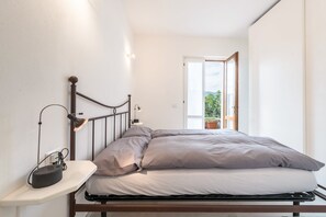 Een enkel bed met hoofdeinde, een nachtkastje met lamp, en uitzicht op de omgeving door een open deur.