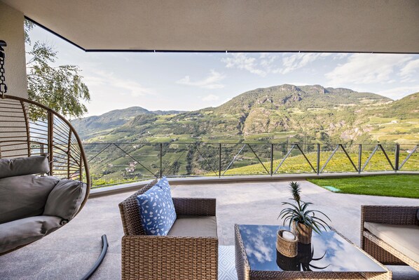 A balcony with wicker furniture, a hanging chair, and a view of a mountainous landscape.