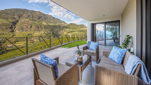 A balcony with wicker furniture, a glass door, and a view of a mountainous landscape.