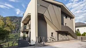 A modern building with a unique angular design, a balcony, and a view of a hilly landscape.
