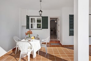 A dining area with a table, chairs, a window with shutters, a hanging light fixture, and a door leading to another room. - Apartment "Atalaya" with Terrace and Sea Views (Conil de la Frontera)