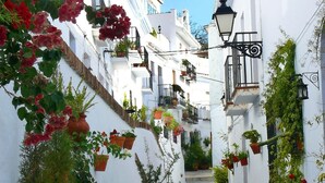 A narrow street with white buildings, balconies with potted plants, and a street lamp. - Apartment Valparaiso - Burriana Beach with Sea View, Pool, Wi-Fi, A/C & Terraces (Nerja)