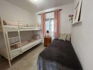 Un lit superposé avec une commode et un lit simple, dans une pièce dotée d’une fenêtre et de rideaux.