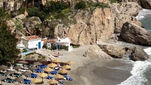 A coastal area with rocky cliffs, a beach with umbrellas, and a small building with a blue door. - Apartment Valparaiso - Burriana Beach with Sea View, Pool, Wi-Fi, A/C & Terraces (Nerja)