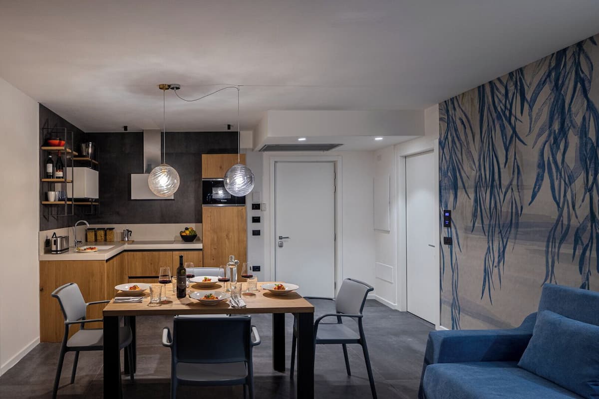 Een moderne eethoek met een houten tafel en stoelen, een keuken op de achtergrond en een blauwe bank.