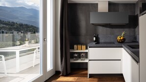 A modern kitchen with a view of the outdoors, a dining area with a table and chairs, and a large window. - Aris Apartments & Sky Pool - Tonelli Hotels - Adults Only (Riva del Garda)