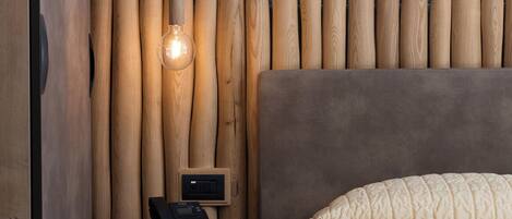 A bedroom with a wooden slat wall, a round bedside table with a telephone, and a bed with a quilted cover.