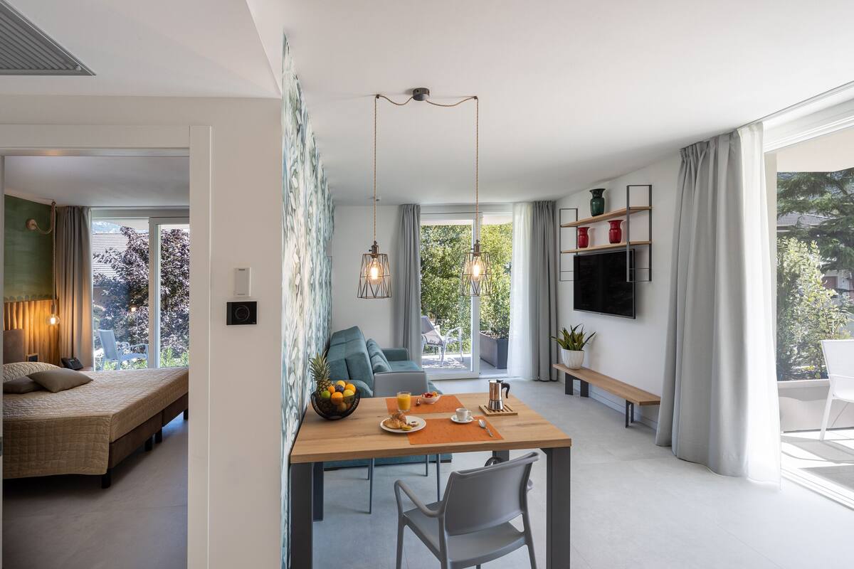 Een moderne woonkamer met een eethoek, een bank, een televisie en een groot raam met gordijnen.