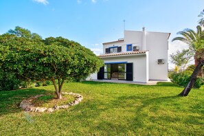A modern two-story house with a white exterior, a balcony, and a well-maintained lawn.