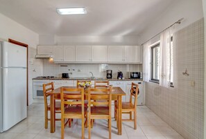 A kitchen with white cabinets, a dining table with chairs, a refrigerator, a microwave, and a window with curtains.